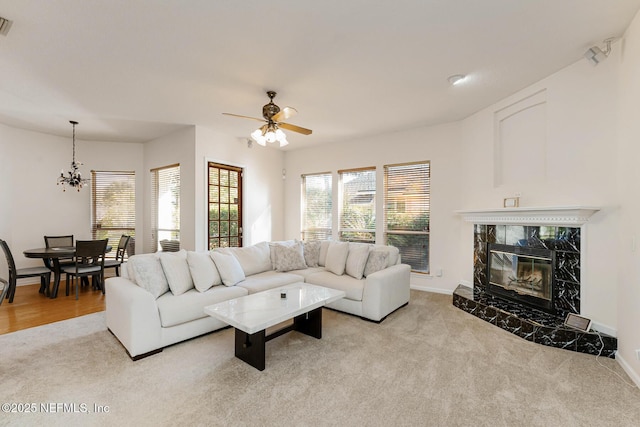 living room with light colored carpet, ceiling fan with notable chandelier, a premium fireplace, visible vents, and baseboards