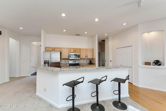 kitchen featuring a spacious island, a breakfast bar area, light stone countertops, stainless steel appliances, and light brown cabinetry