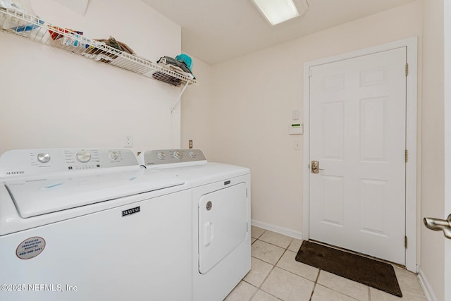 clothes washing area featuring light tile patterned floors, laundry area, washing machine and dryer, and baseboards