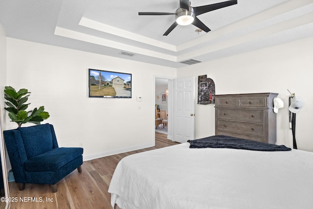 bedroom featuring hardwood / wood-style flooring, ceiling fan, and a tray ceiling