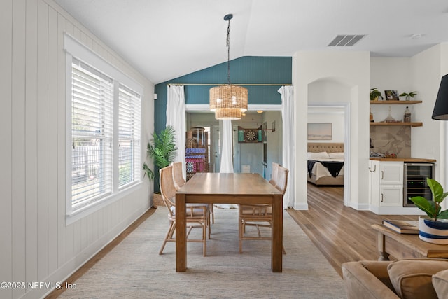 dining room featuring lofted ceiling, light wood-type flooring, beverage cooler, a chandelier, and indoor bar