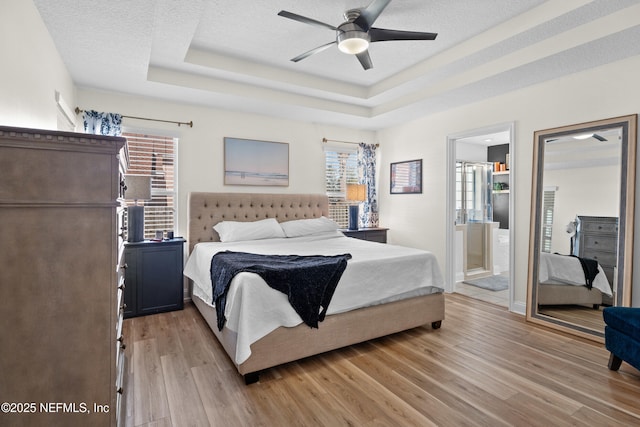 bedroom featuring multiple windows, a raised ceiling, a textured ceiling, and light wood-type flooring