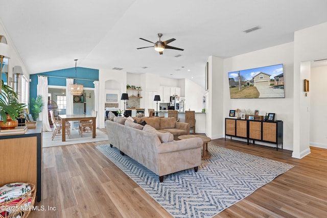 living room with vaulted ceiling, ceiling fan with notable chandelier, and light hardwood / wood-style floors