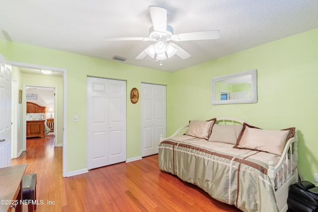 bedroom featuring ceiling fan, light hardwood / wood-style floors, and two closets