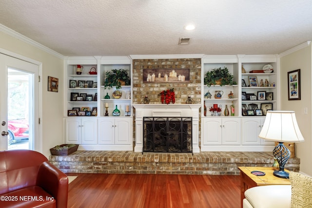 living room with built in shelves, a brick fireplace, a textured ceiling, ornamental molding, and hardwood / wood-style floors