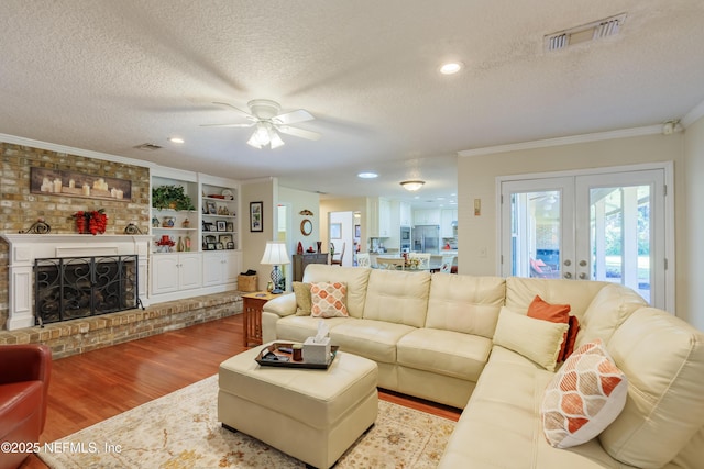 living room featuring crown molding, a brick fireplace, light hardwood / wood-style floors, and a textured ceiling