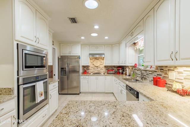 kitchen with sink, white cabinets, light stone counters, stainless steel appliances, and wall chimney exhaust hood