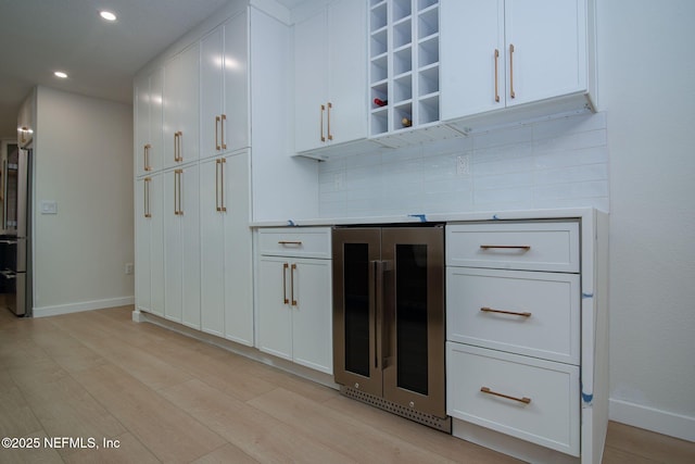 bar featuring white cabinetry, tasteful backsplash, beverage cooler, and light hardwood / wood-style flooring