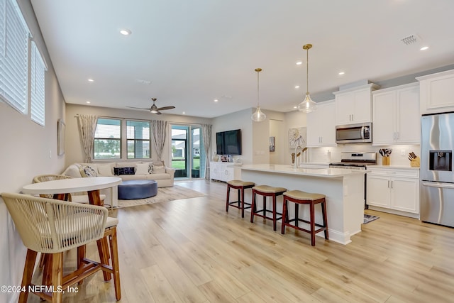 kitchen featuring white cabinetry, hanging light fixtures, a center island with sink, a kitchen breakfast bar, and stainless steel appliances