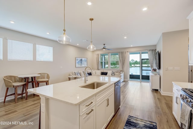 kitchen featuring sink, a kitchen island with sink, white cabinetry, hanging light fixtures, and stainless steel appliances