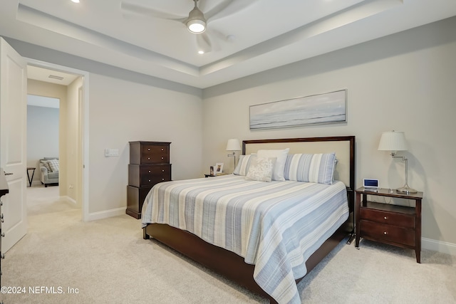 bedroom with light colored carpet, a raised ceiling, and ceiling fan