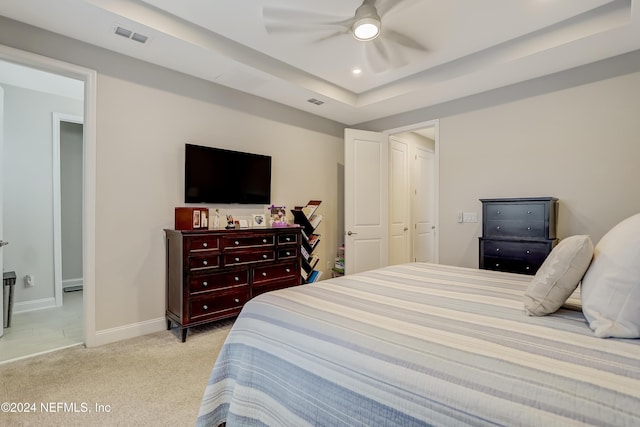 bedroom with ceiling fan, light colored carpet, and a raised ceiling