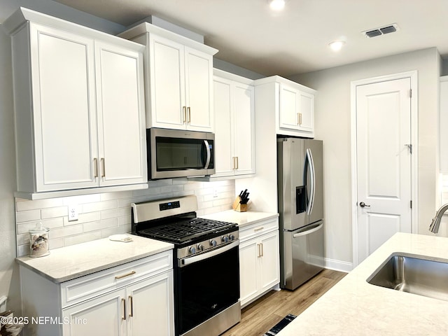 kitchen with sink, white cabinetry, light stone counters, tasteful backsplash, and appliances with stainless steel finishes