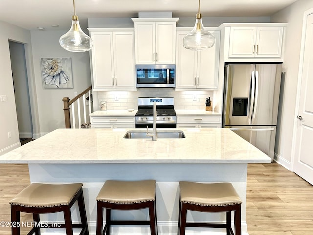 kitchen featuring tasteful backsplash, white cabinetry, light stone counters, stainless steel appliances, and a center island with sink