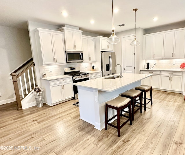 kitchen with decorative light fixtures, white cabinetry, sink, a kitchen island with sink, and stainless steel appliances