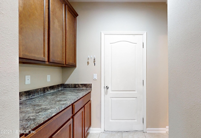 interior space featuring light tile patterned floors, baseboards, dark stone countertops, and brown cabinets