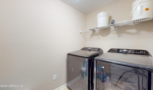 clothes washing area with a textured ceiling, washing machine and dryer, laundry area, baseboards, and tile patterned floors