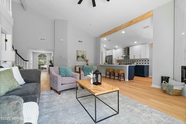 living room with beam ceiling, high vaulted ceiling, ceiling fan, and light wood-type flooring