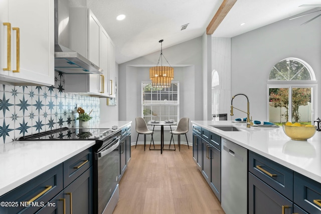 kitchen featuring hanging light fixtures, appliances with stainless steel finishes, wall chimney range hood, and white cabinets