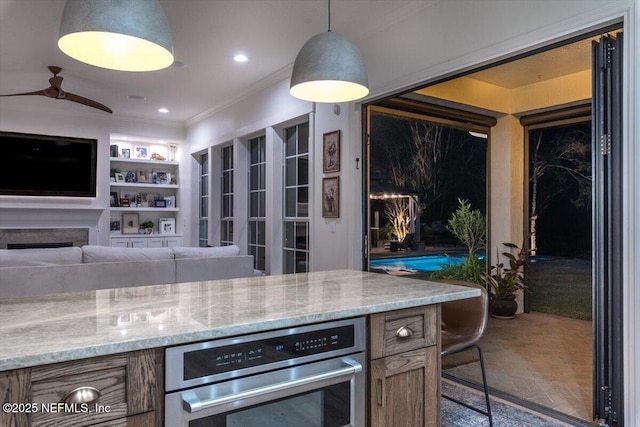 kitchen featuring recessed lighting, crown molding, stainless steel oven, light stone countertops, and hanging light fixtures