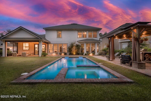 back of property at dusk featuring a pool with connected hot tub, a gazebo, outdoor lounge area, a yard, and a patio area