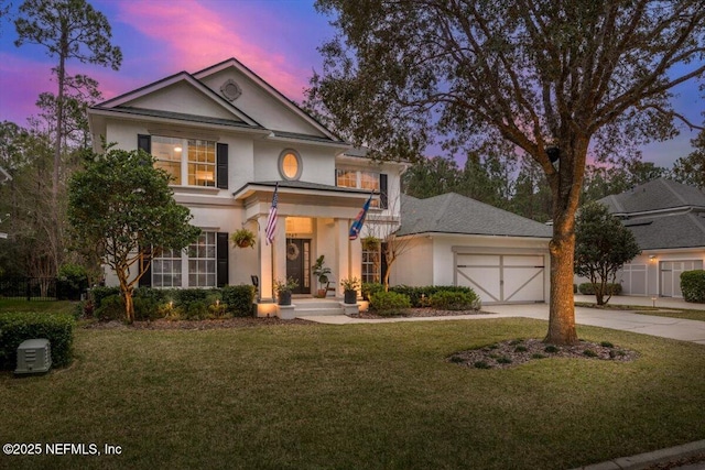 greek revival house featuring concrete driveway, a garage, a front yard, and stucco siding