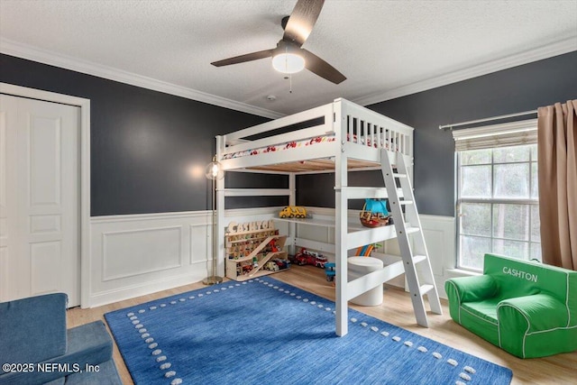 bedroom featuring crown molding, ceiling fan, a wainscoted wall, wood finished floors, and a textured ceiling