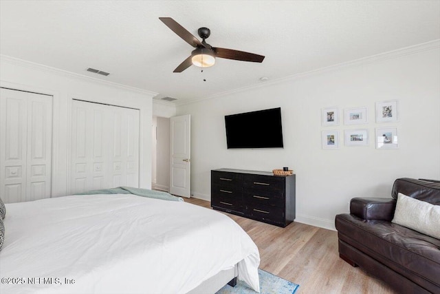 bedroom with visible vents, light wood-style flooring, ceiling fan, ornamental molding, and two closets