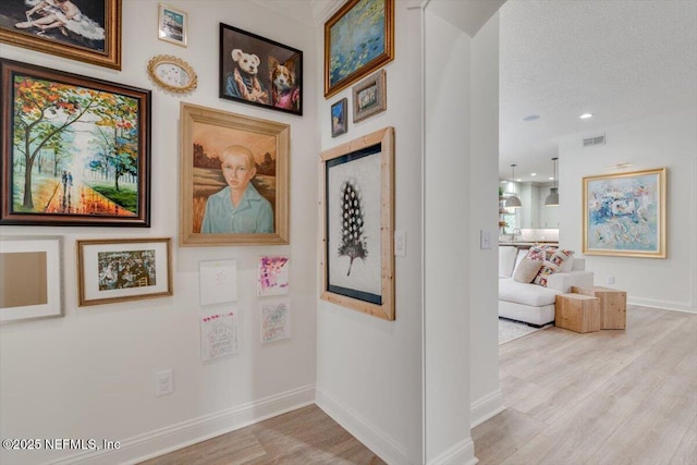 hallway featuring visible vents, baseboards, a textured ceiling, and wood finished floors