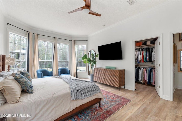 bedroom featuring a spacious closet, visible vents, crown molding, light wood-style floors, and a textured ceiling