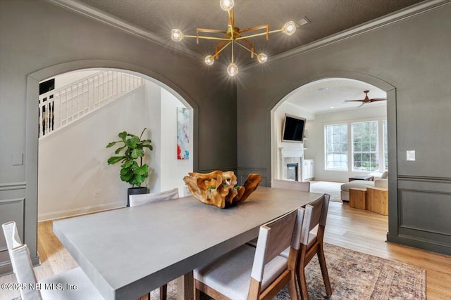 dining area with a textured ceiling, light wood-style flooring, a fireplace, and ornamental molding