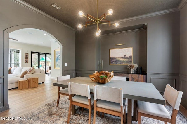 dining room with a wainscoted wall, ornamental molding, wood finished floors, arched walkways, and a decorative wall