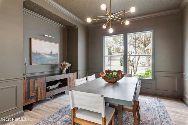 dining space featuring light wood finished floors, a textured ceiling, crown molding, and a decorative wall