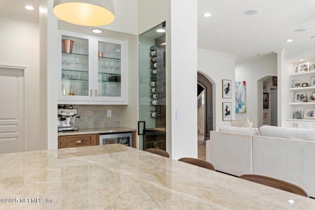 interior space featuring built in shelves, arched walkways, ornamental molding, decorative backsplash, and glass insert cabinets