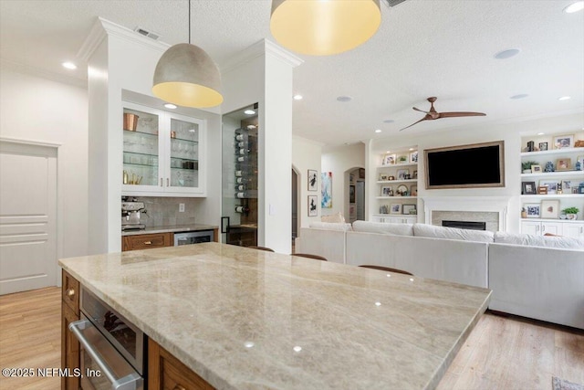 kitchen with visible vents, a textured ceiling, light wood-style floors, a fireplace, and light stone countertops