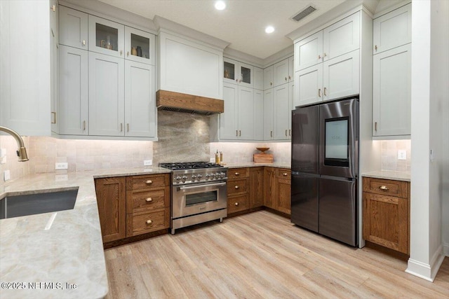 kitchen featuring light wood finished floors, visible vents, light stone counters, stainless steel appliances, and a sink