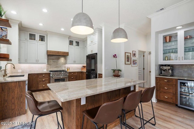 kitchen featuring black refrigerator, custom range hood, light stone counters, high end stainless steel range oven, and a sink