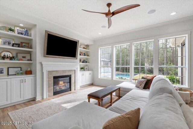 living area with crown molding, light wood-style flooring, a high end fireplace, and a textured ceiling