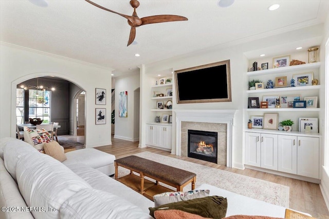 living area featuring a glass covered fireplace, built in features, arched walkways, and light wood finished floors