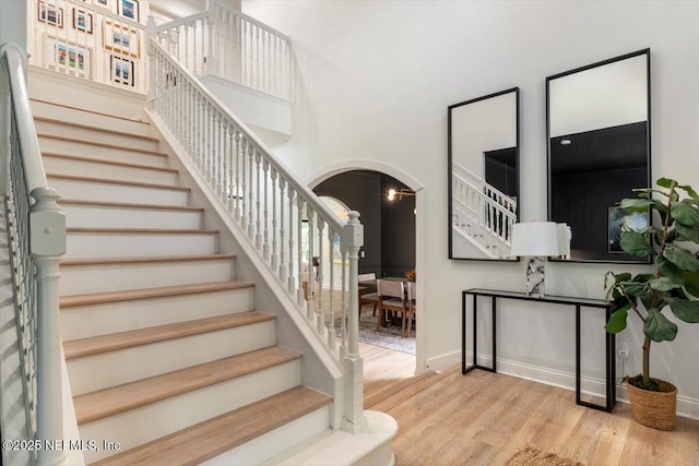stairs with baseboards, arched walkways, a high ceiling, and wood finished floors