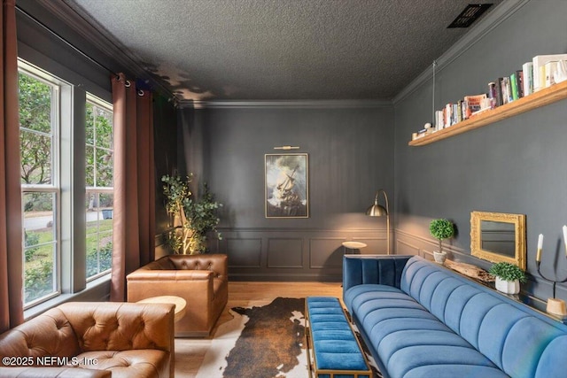 living area with wood finished floors, visible vents, ornamental molding, a textured ceiling, and a decorative wall