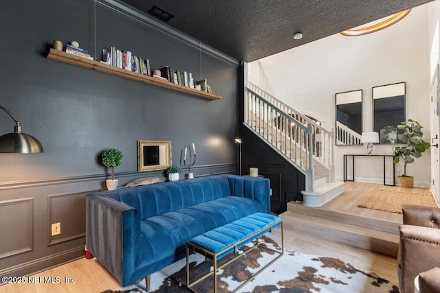 living area featuring visible vents, a textured ceiling, wood finished floors, stairway, and a decorative wall