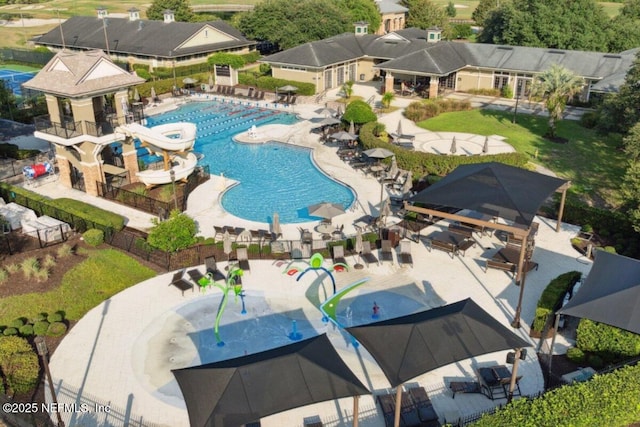 community pool with a patio area, a water play area, a water slide, and fence