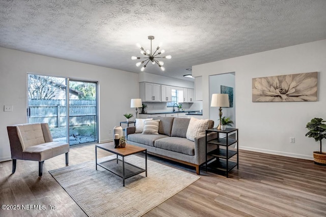 living room featuring an inviting chandelier, sink, light hardwood / wood-style flooring, and a textured ceiling