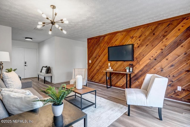 living room with wood-type flooring, a chandelier, a textured ceiling, and wood walls