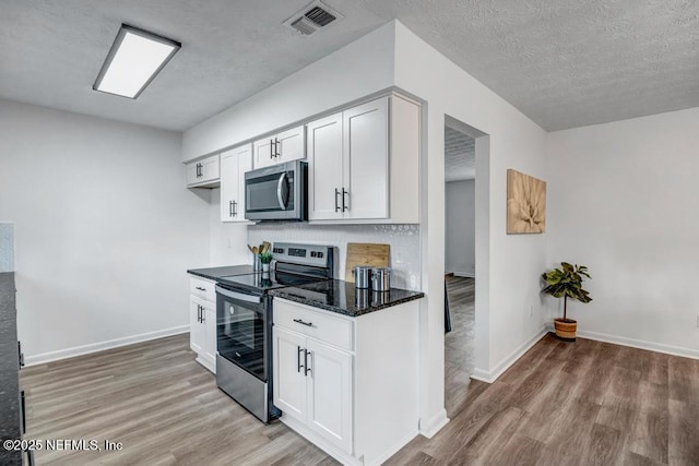 kitchen with white cabinetry, hardwood / wood-style floors, dark stone countertops, stainless steel appliances, and a textured ceiling