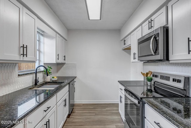 kitchen with dark stone countertops, stainless steel appliances, sink, and white cabinets