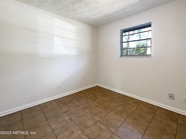 spare room featuring a textured ceiling, dark tile patterned floors, and baseboards