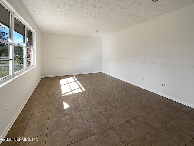 empty room with a textured ceiling, dark tile patterned floors, and baseboards