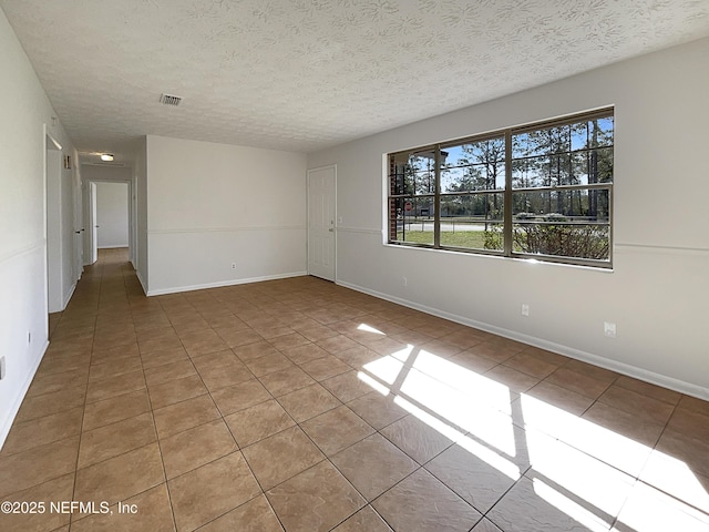 unfurnished room with light tile patterned floors, a textured ceiling, visible vents, and baseboards